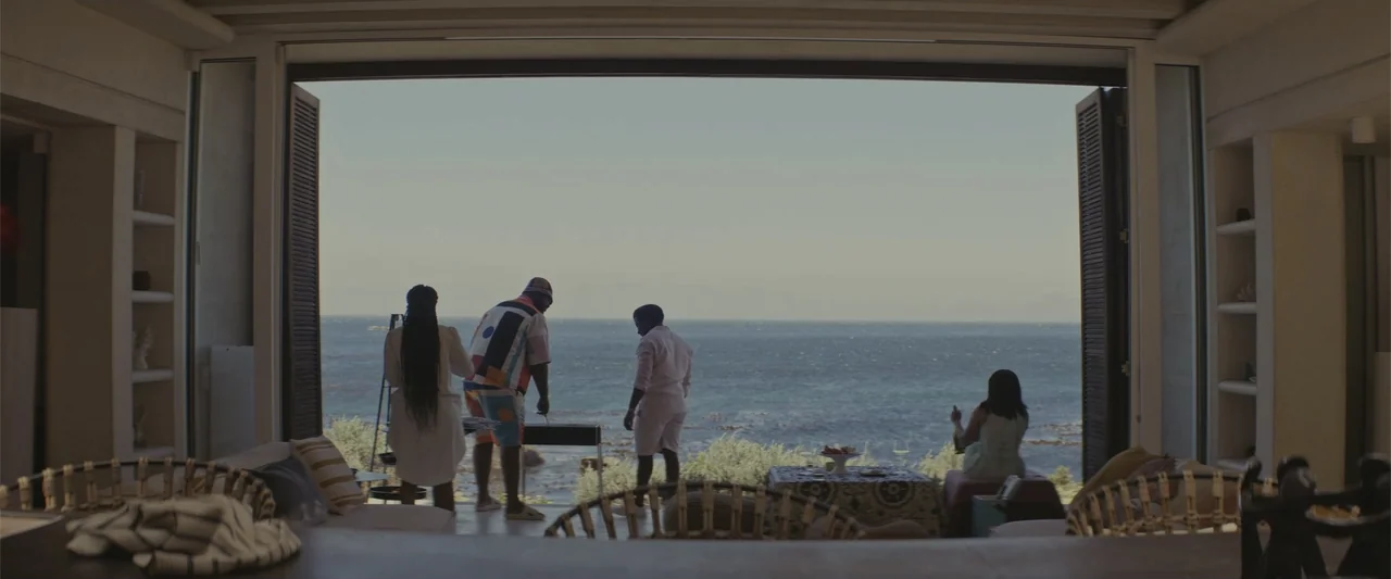 A Scam Called Love (2025) movie still: wide — A luxury open-plan living space opens onto a sunlit patio overlooking the ocean. Four individuals…