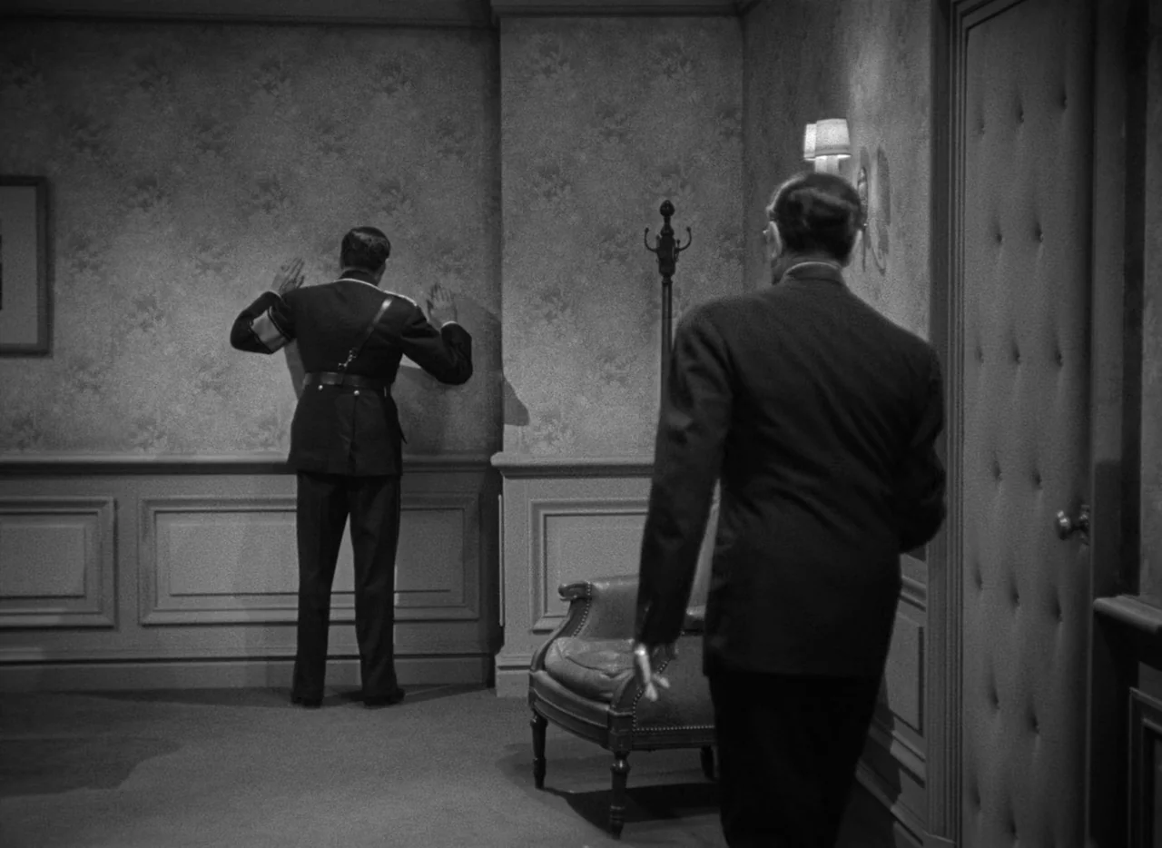 To Be or Not To Be (1942) movie still: wide — A formal interior with patterned wallpaper and dark wood wainscoting. A man in uniform faces the wall…