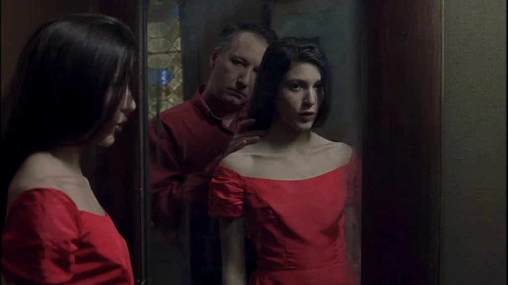 Romance (1999) movie still: medium — A woman stares into a reflective surface while a man stands directly behind her. The man rests his hand on her…