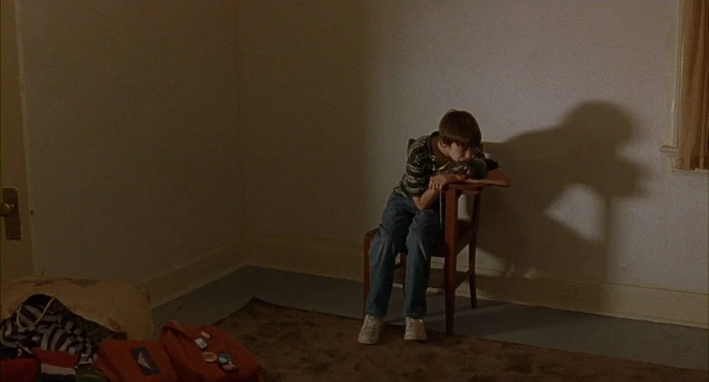 The Squid and the Whale (2005) movie still: wide — A sparsely furnished room features beige walls, brown carpeting, and an empty corner. A young boy…