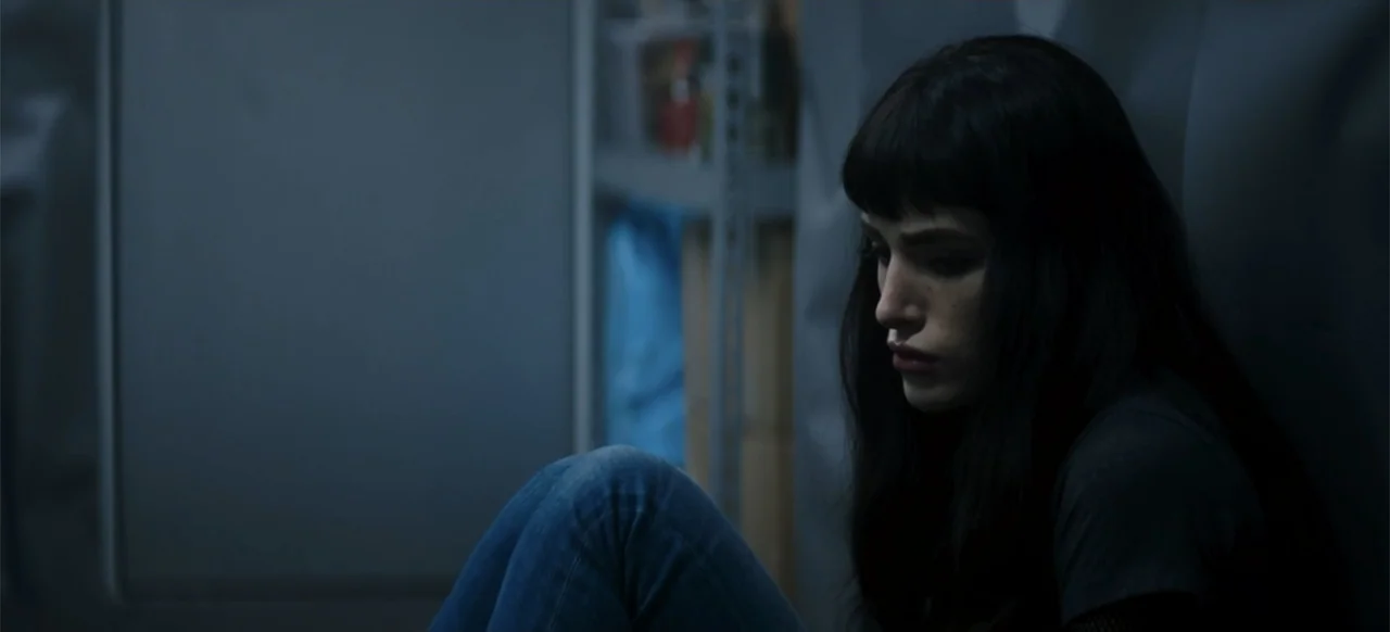 I Still See You (2018) movie still: medium — A dimly lit storage room has metal shelving units visible in the background. A woman sits on the floor…