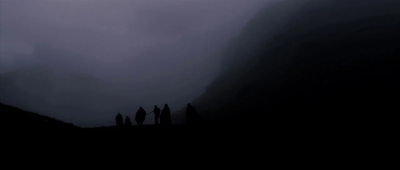 Valhalla Rising (2009) movie still: wide — A group of figures walks along a rocky ridge against misty, dark mountains. The terrain is rugged and…