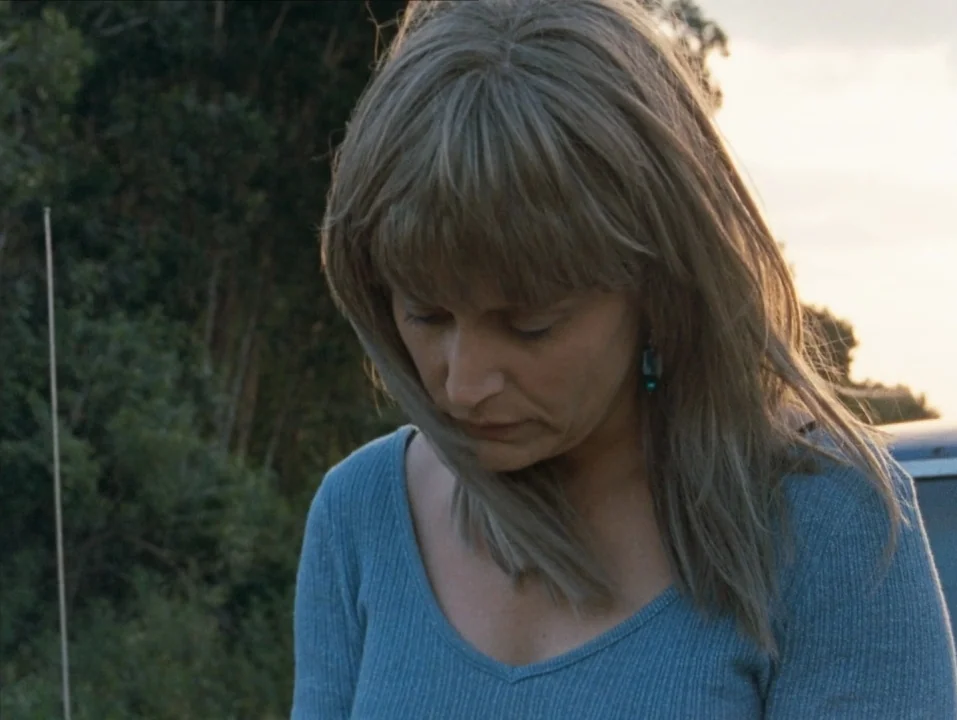 River of Grass (1994) movie still: closeup — A woman stands outdoors in a rural, open-air environment during the late afternoon. She gazes downward…