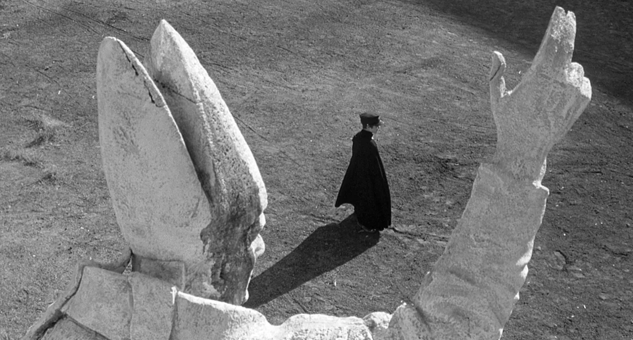 8 1/2 (1963) movie still: wide — A vast, empty stretch of hard-packed earth features an oversized stone statue sculpture. A lone figure dressed in…