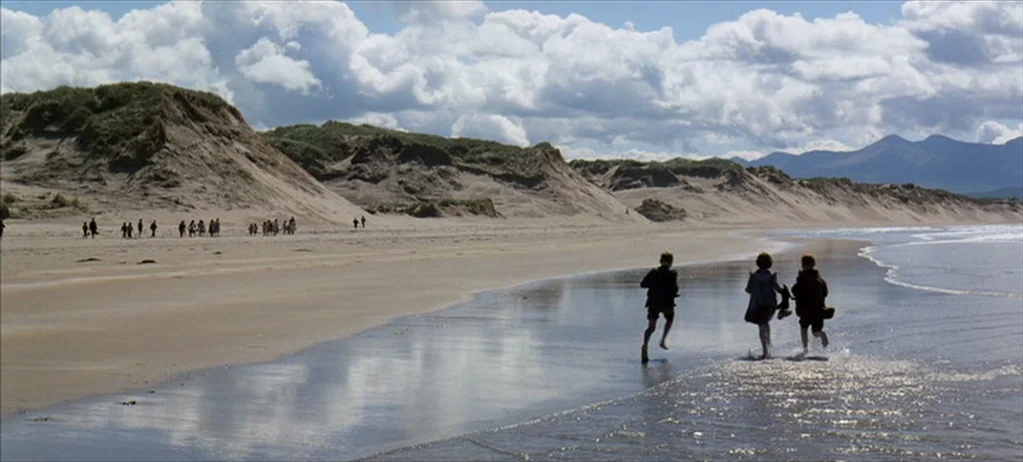 Ryan’s Daughter (1970) movie still: wide — A wide, expansive coastal landscape features vast sand dunes under a large, cloudy sky. Three children…
