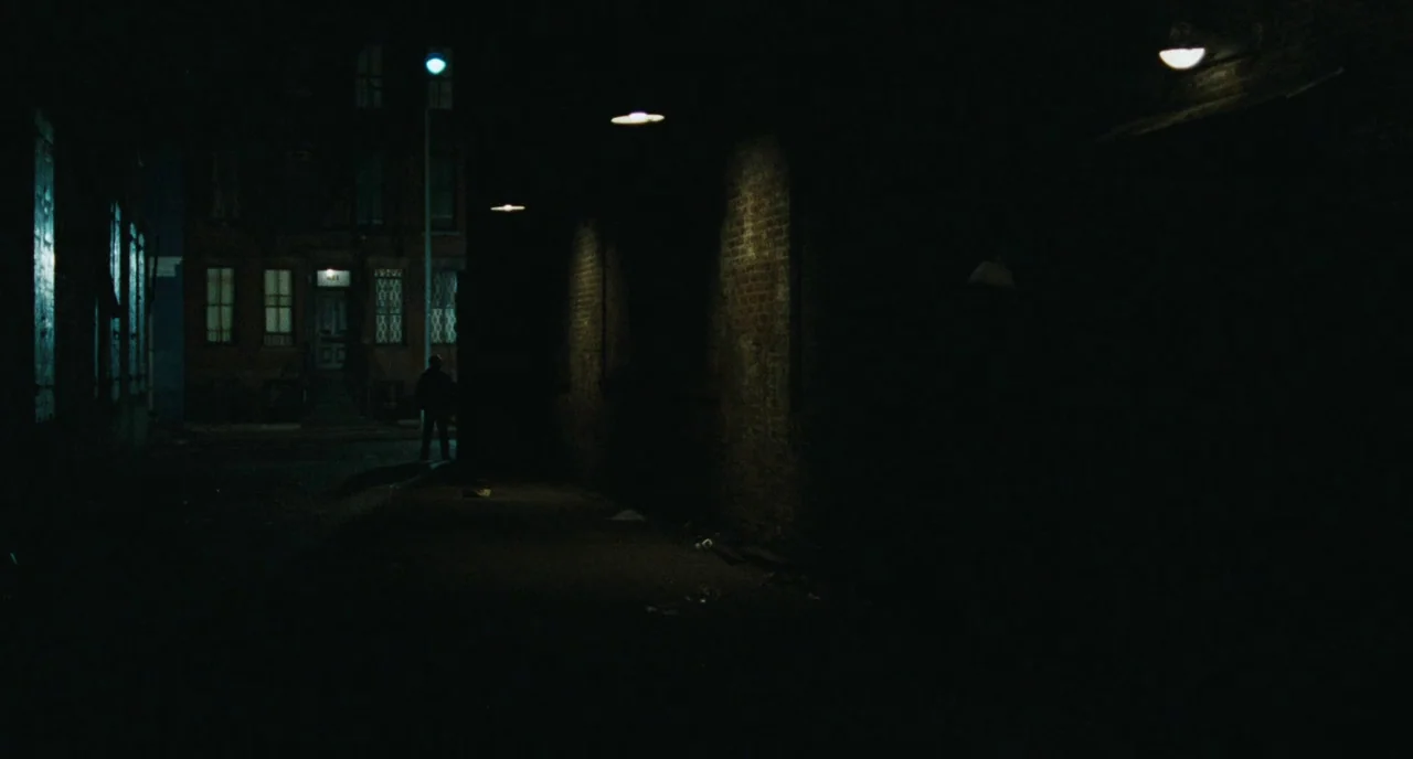 The Panic in Needle Park (1971) movie still: wide — A dark, narrow city alley is illuminated by sparse overhead streetlights. A solitary figure…