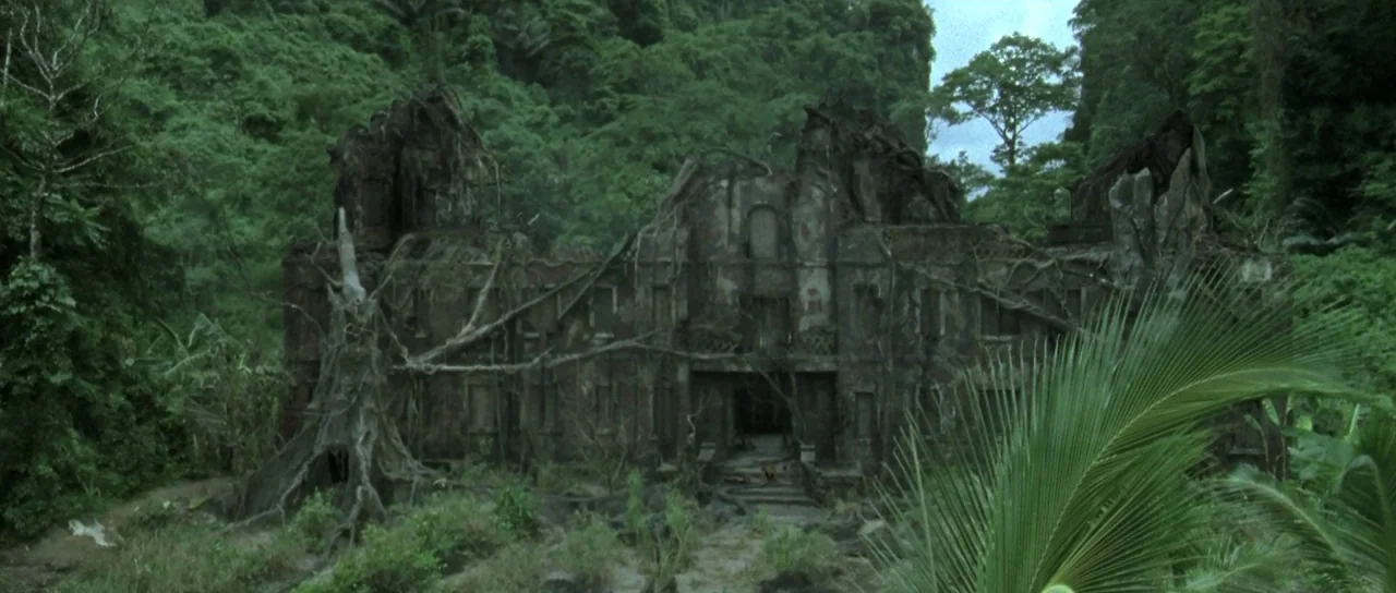 Vinyan (2008) movie still: establishing — A dilapidated multi-story mansion stands overgrown with vines in a dense tropical rainforest. Large dead…