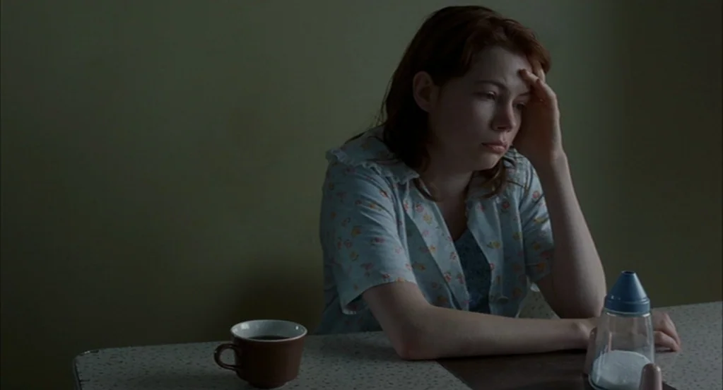 Brokeback Mountain (2005) movie still: medium — A woman sits at a vintage table with a simple floral patterned shirt. She rests her head on her hand…