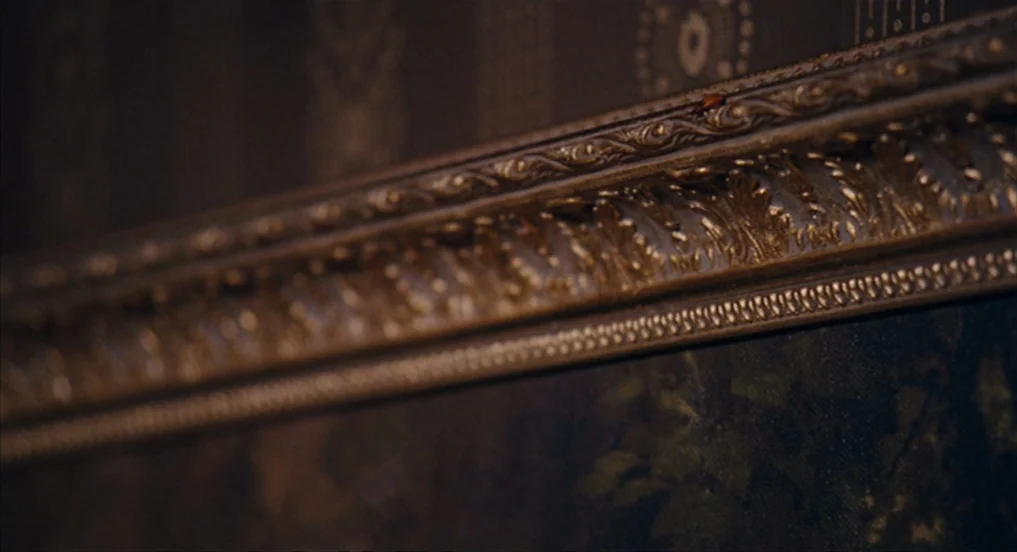 House of Tolerance (2011) movie still: closeup — A close-up view shows a portion of an ornate, dark gold picture frame. A tiny insect walks along…