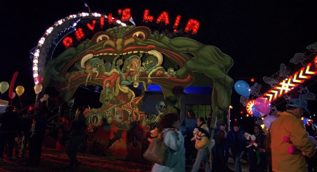 Child’s Play 3 (1991) movie still: wide — A nighttime carnival midway features a large painted attraction entrance titled Devil's Lair. People walk…