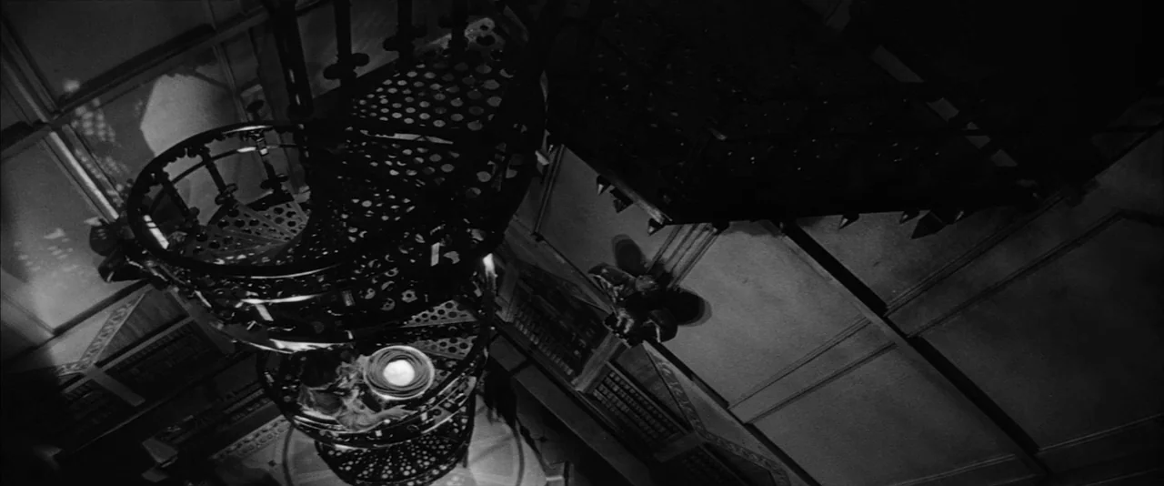 The Haunting (1963) movie still: wide — A Victorian-era ornate metal spiral staircase descends into a dark floor. The architectural structure…