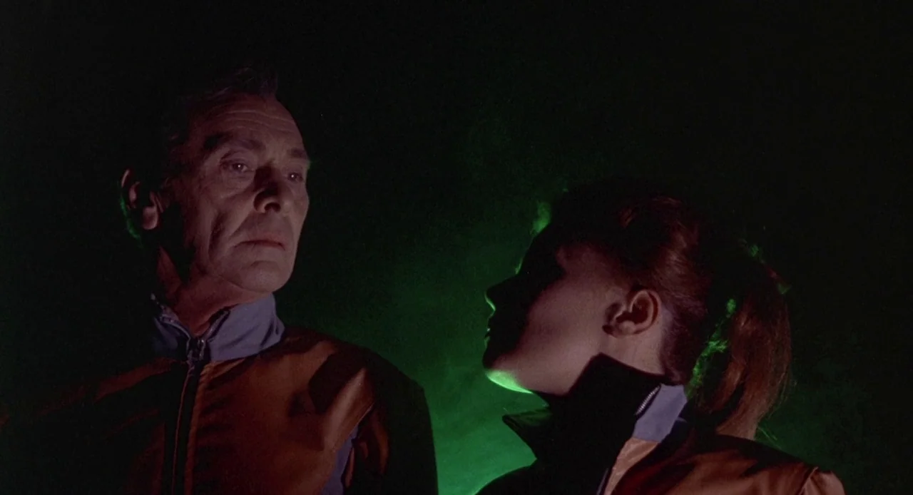 Planet of the Vampires (1965) movie still: medium — Two individuals stand in a dimly lit space with a strong green light source. They are wearing…