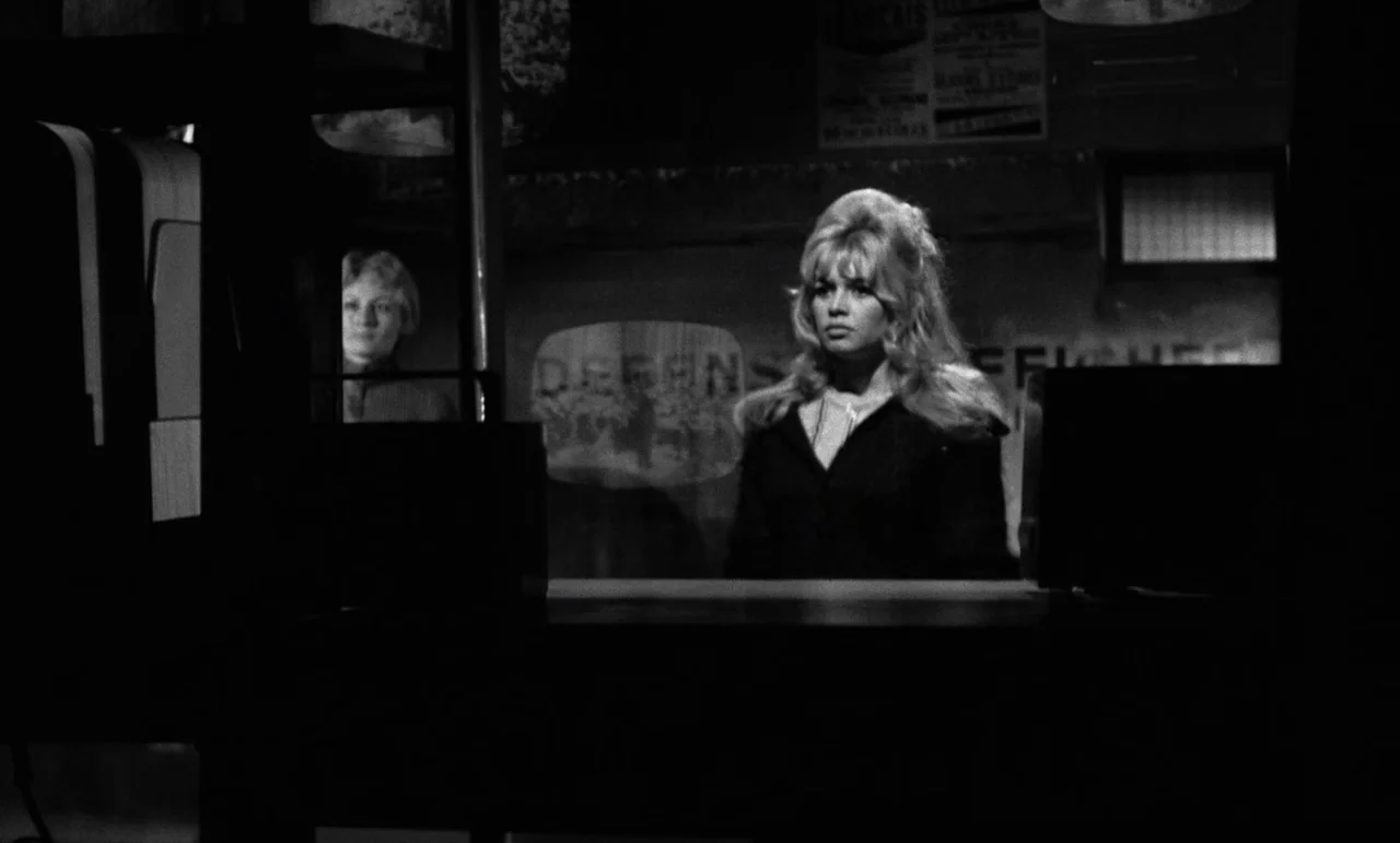 La Verite (1960) movie still: medium — A dimly lit indoor service area features a blonde woman behind a counter. A second woman stands in the…