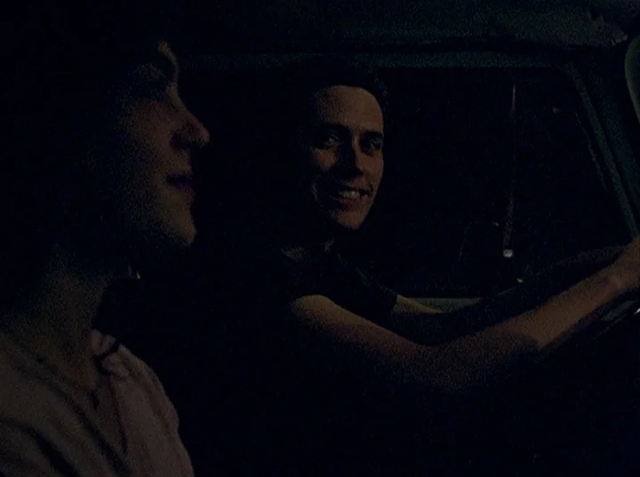 Slacker (1991) movie still: medium — The interior of a vehicle at night with minimal external light sources. A driver looks toward his passenger…
