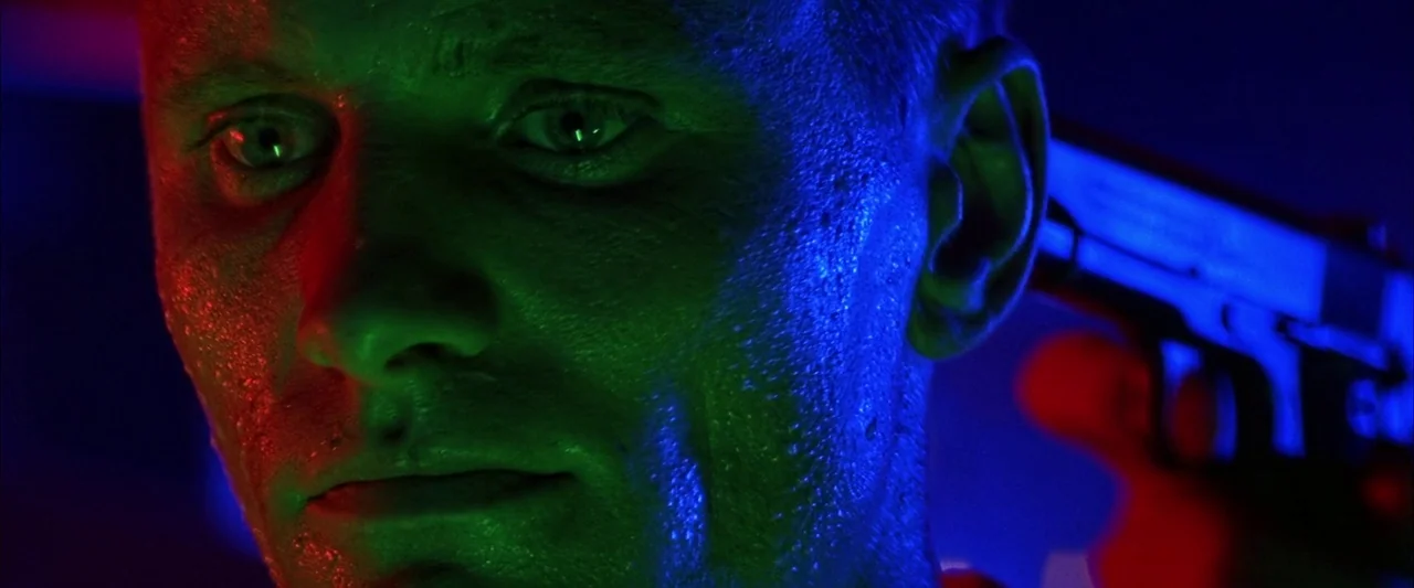 Crimson Tide (1995) movie still: closeup — A man's face is illuminated by sharp blue and green light in a dark space. He looks toward the camera…