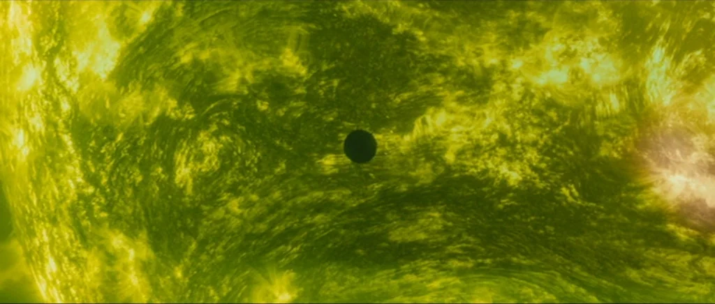 Sunshine movie still: establishing — A textured yellow and green solar surface fills the frame with swirling plasma patterns. A small perfectly…