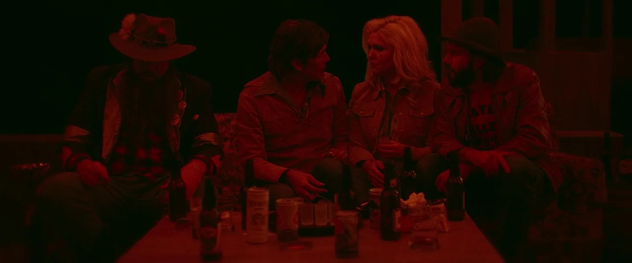 Blaze (2018) movie still: medium — A group of four adults sits on a couch in a dimly lit room. The environment is heavily saturated in deep red…