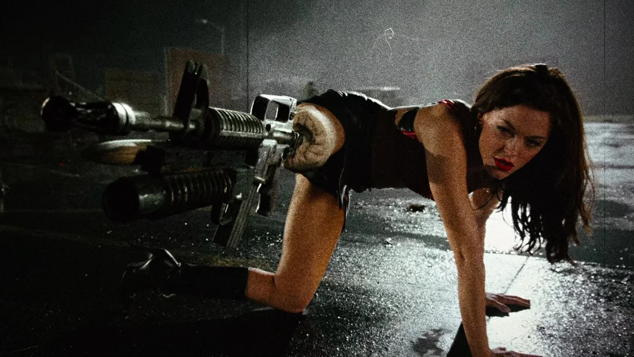 Planet Terror (2007) movie still: medium — A dark paved outdoor lot at night with wet surfaces under artificial illumination. A young woman in dark…