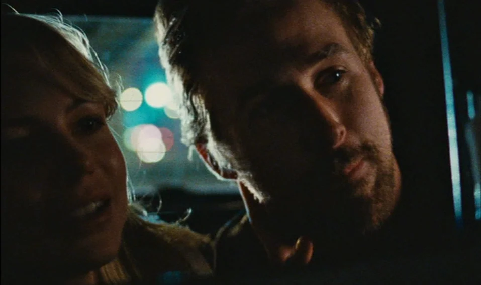 Blue Valentine (2010) movie still: closeup — The interior of a car at night with blurred city lights in the background. A man and woman sit next to…