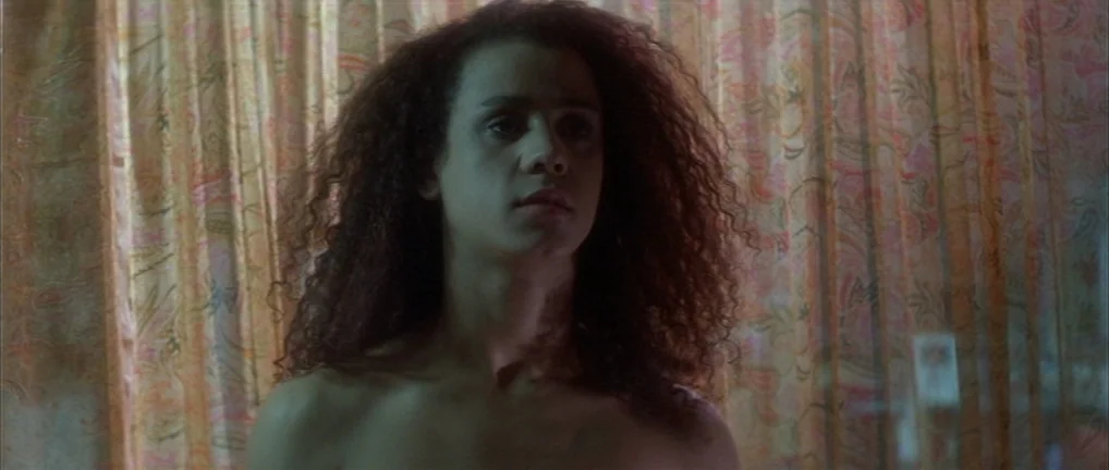 The Crying Game (1992) movie still: medium — A woman stands before a set of thin, patterned curtains in a dimly lit room. She looks forward while…