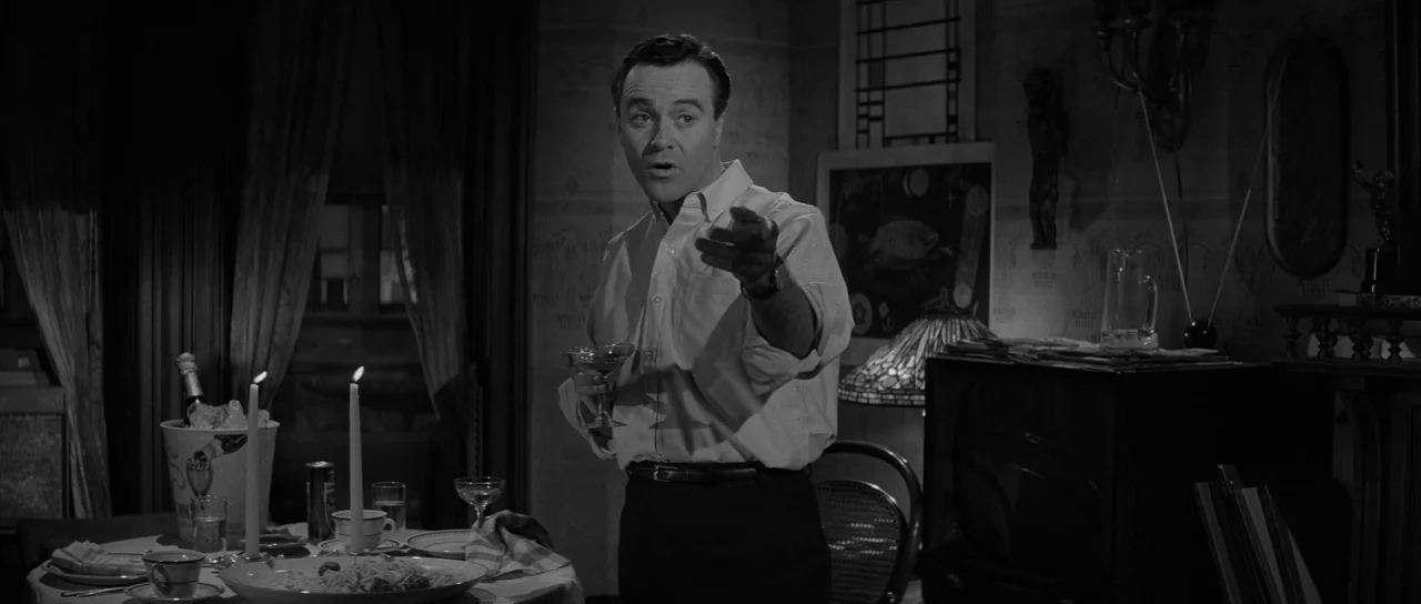The Apartment (1960) movie still: medium — A dimly lit room features a dining table set with plates and candles. A man in a buttoned shirt gestures…