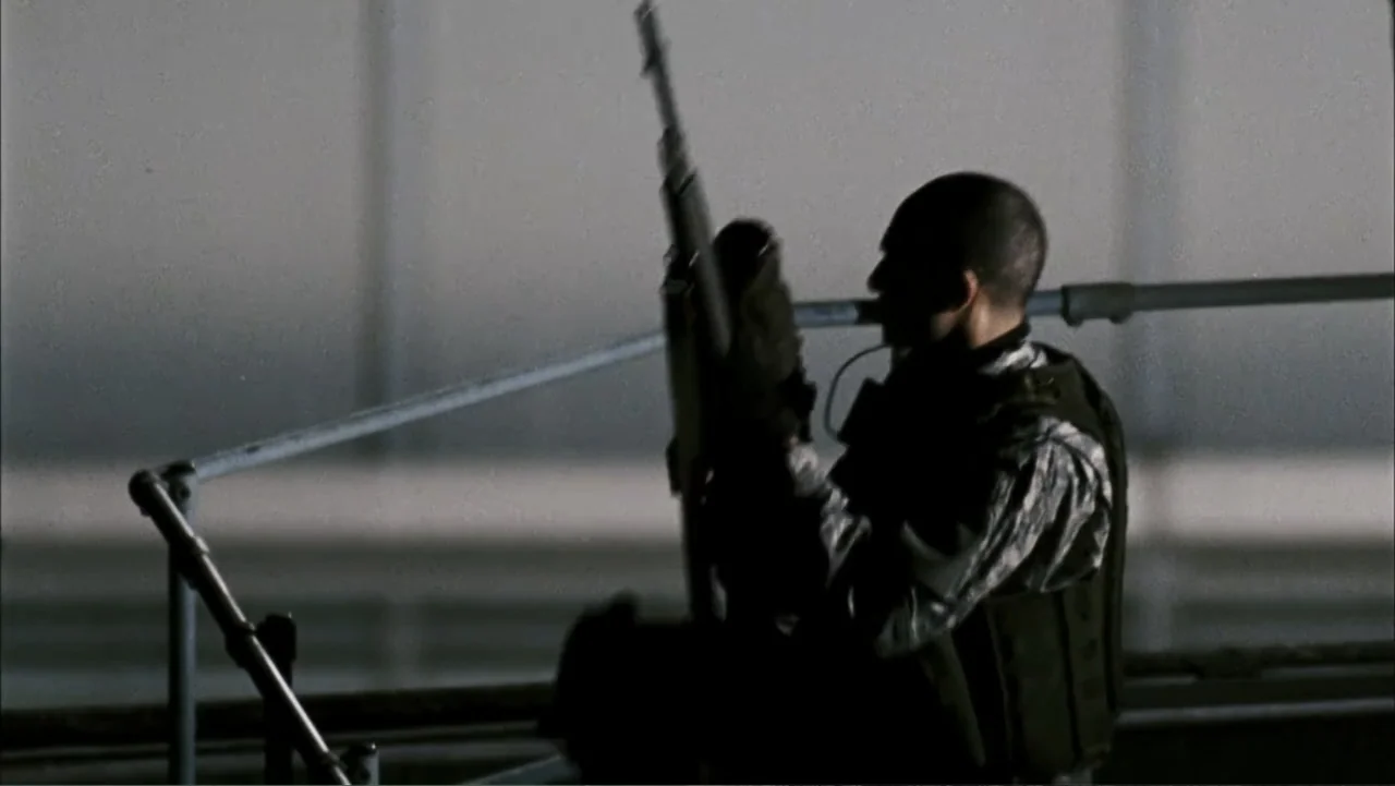 28 Weeks Later (2007) movie still: medium — A dark metal balcony railing overlooks a dim and expansive industrial space. A lone soldier in tactical…