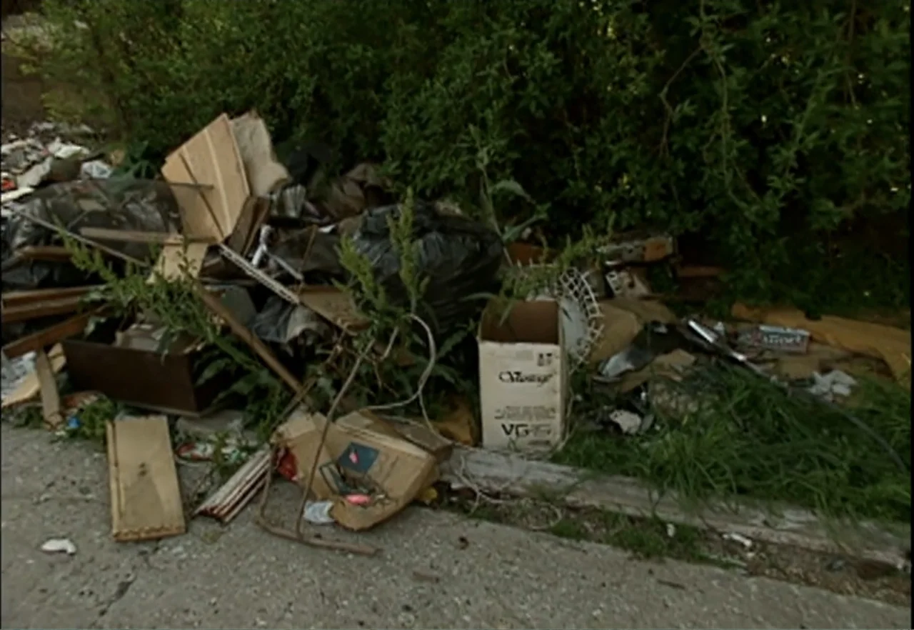 Broken Child (2000) movie still: wide — An outdoor area features a chaotic pile of discarded household waste and debris. Cardboard boxes, plastic…