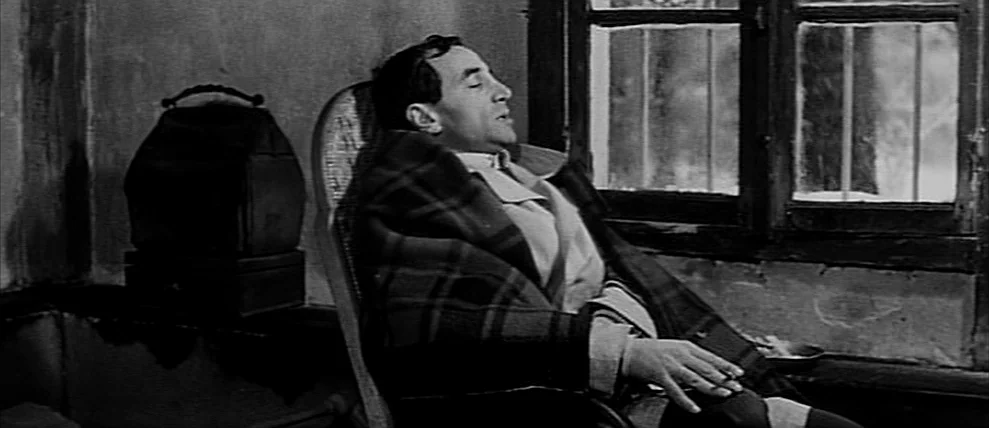 Shoot The Piano Player (Tirez Sur Le Pianiste) (1960) movie still: medium — A man sits in a wooden chair near a window with a barred view. He is…