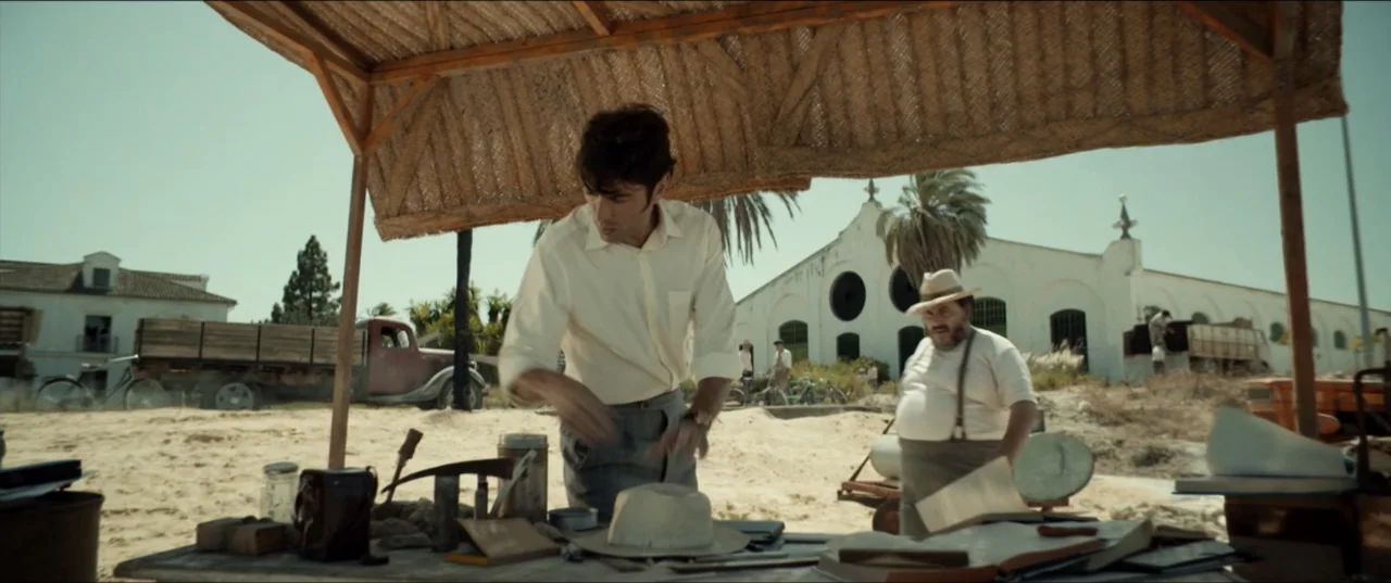 Hear Me: Our Summer (2024) movie still: medium — An arid archaeological site features a straw-roofed workstation under the bright midday sun. Two…