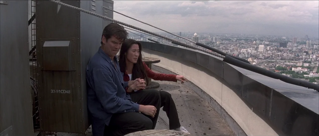 Tomorrow Never Dies (1997) movie still: medium — A metal-clad ledge atop a tall building overlooks a sprawling cityscape under overcast skies. A man…