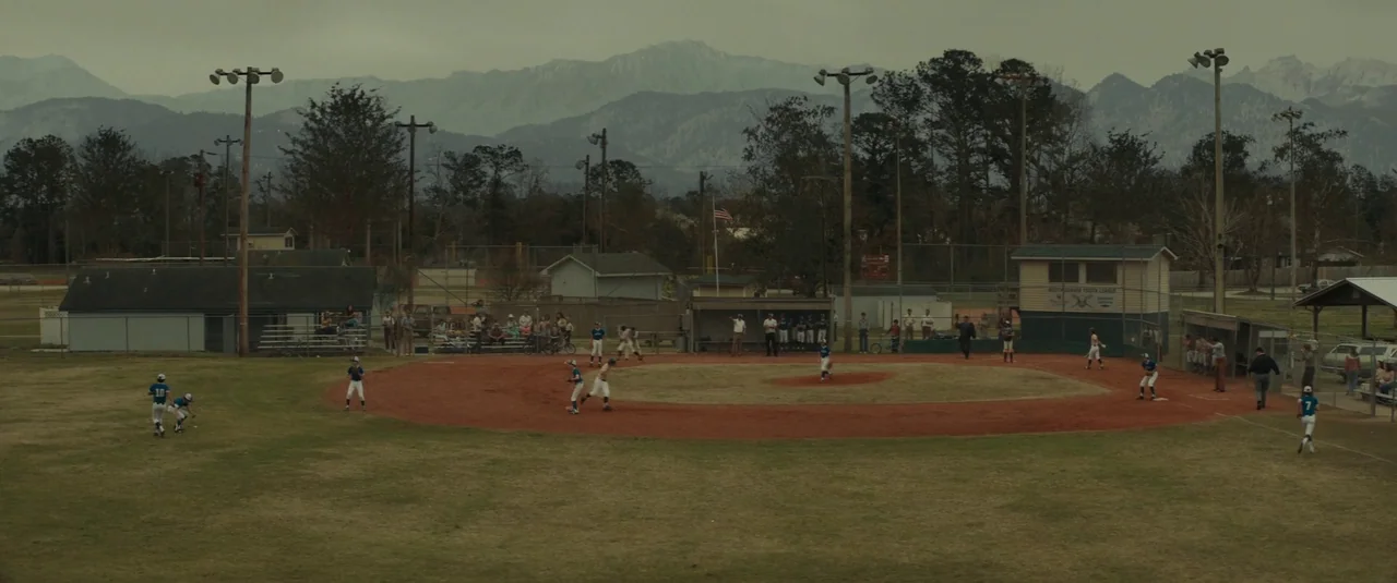 The Black Phone (2021) movie still: wide — A rural baseball field with red dirt sits before a range of distant mountains. Multiple baseball players…