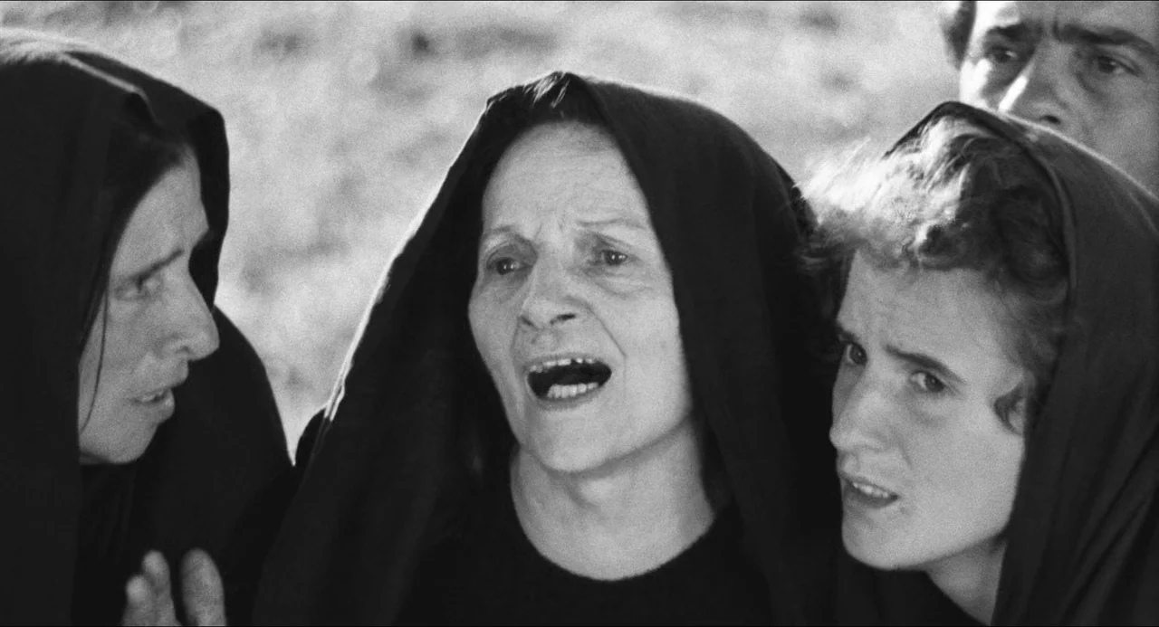 The Gospel According To St. Matthew (1964) movie still: medium — A group of women stand outdoors wearing black head coverings against a blurred…
