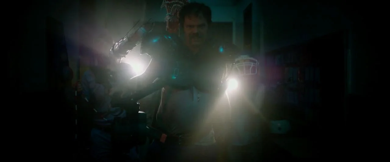 Cooties (2014) movie still: medium — A dark, dimly lit institutional hallway with indistinct objects on either side. A man wearing football shoulder…