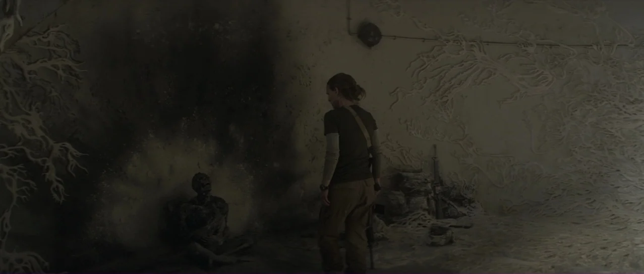 Annihilation (2018) movie still: medium — A dimly lit bunker interior features organic, root-like growths sprawling across the walls. A lone figure…