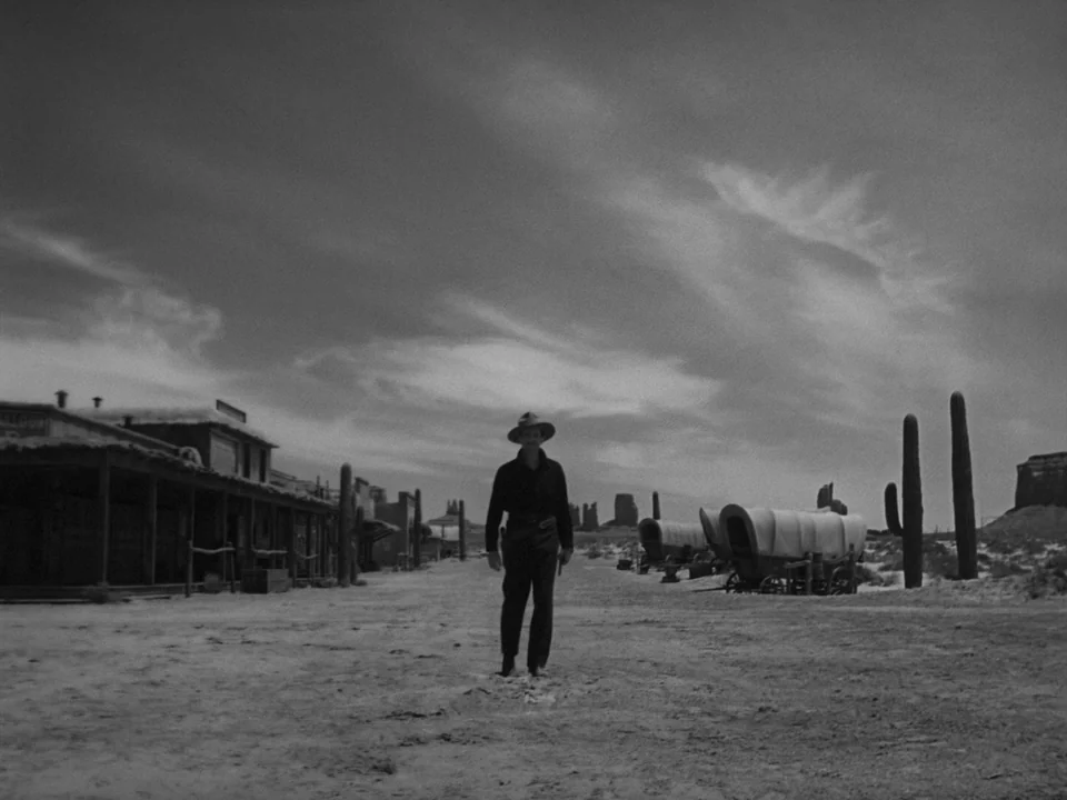 My Darling Clementine (1946) movie still: fullbody — A desolate desert town featuring wooden storefronts and covered wagons under a cloudy sky. A…