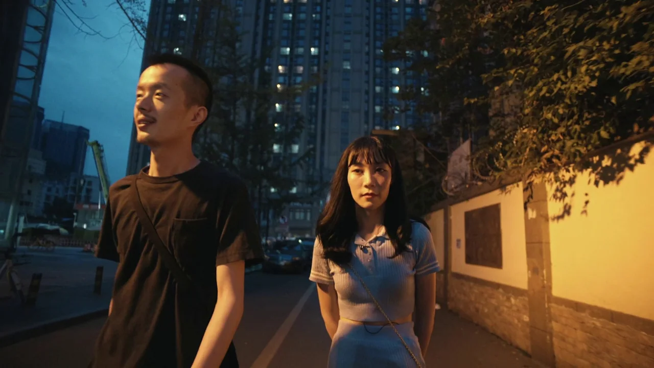 The Last Year of Darkness (2023) movie still: medium — An urban outdoor setting at night features a street bordered by a wall and buildings. A man…
