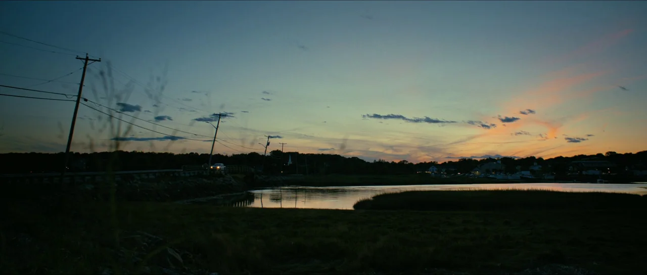 American Fiction (2023) movie still: establishing — A salt marsh with calm water stretches toward a distant coastline during sunset hours. Several…