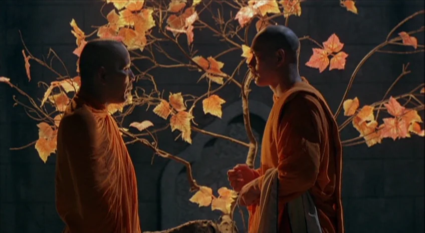 Boxer’s Omen (Mo) (1983) movie still: medium — Two Buddhist monks stand in an dimly lit stone room with a decorative tree. The tree features vibrant…