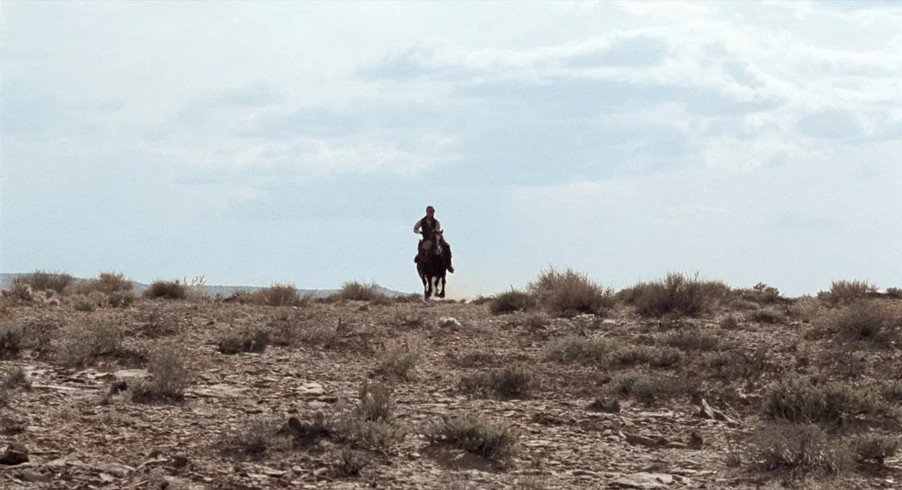 The Shooting (1966) movie still: wide — A wide, arid desert expanse features rocky ground sparsely covered with small shrubs. A solitary man on…