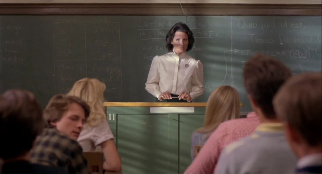 Teen Wolf (1985) movie still: medium — A traditional classroom features a large green chalkboard covered in Latin grammar text. A female teacher…
