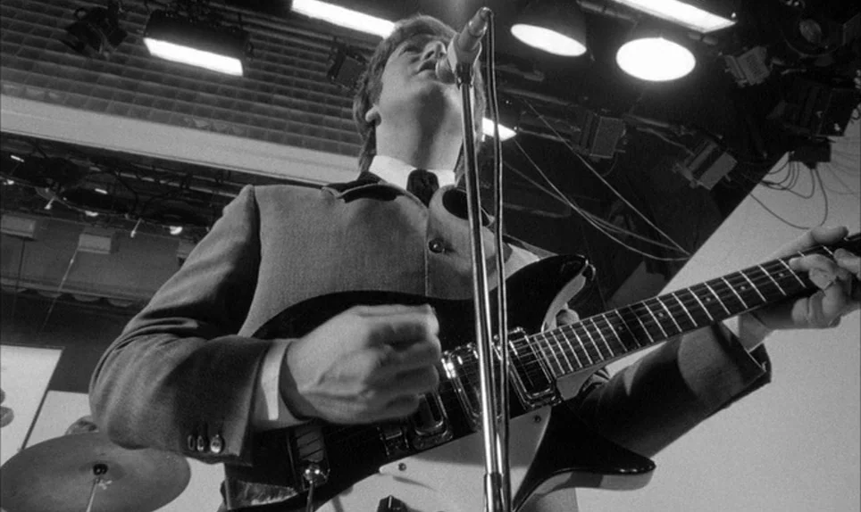 A Hard Days Night (1964) movie still: medium — A television studio interior with multiple overhead stage lights visible in the background. A man in…