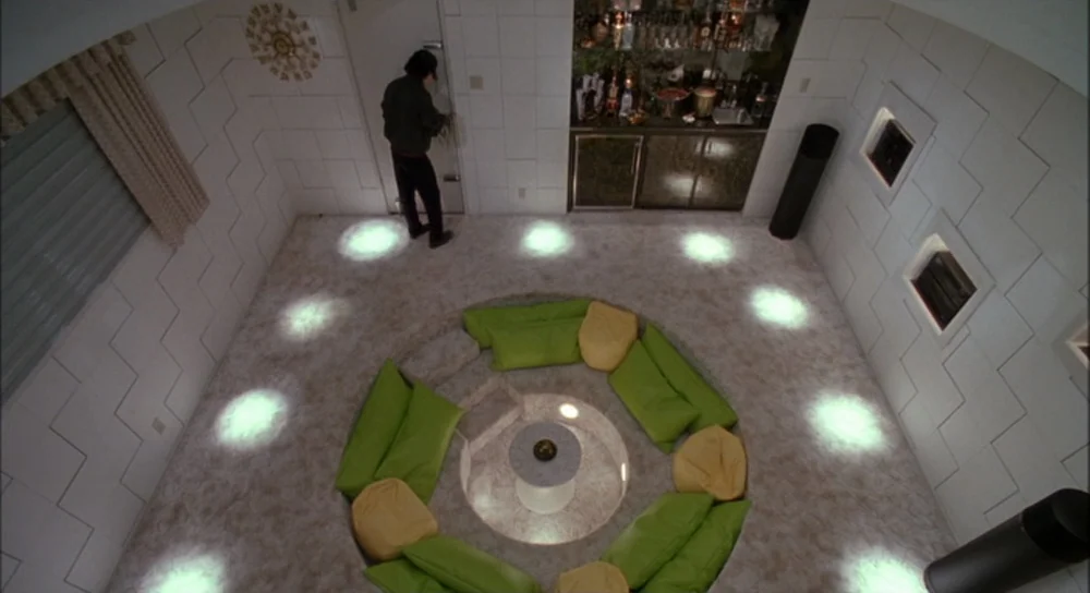 Edward Scissorhands (1990) movie still: wide — A 1970s conversation pit features white tiled walls and a recessed circular seating area. A man…
