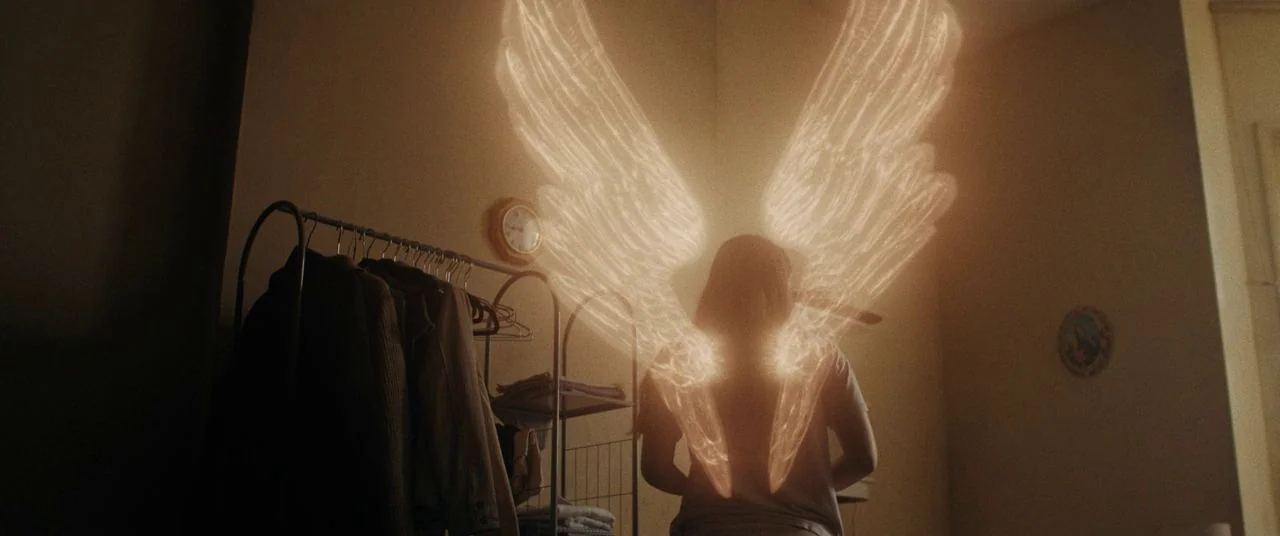 Saint Maud (2019) movie still: medium — A dimly lit room features a clothing rack holding several jackets against a corner wall. A person stands…