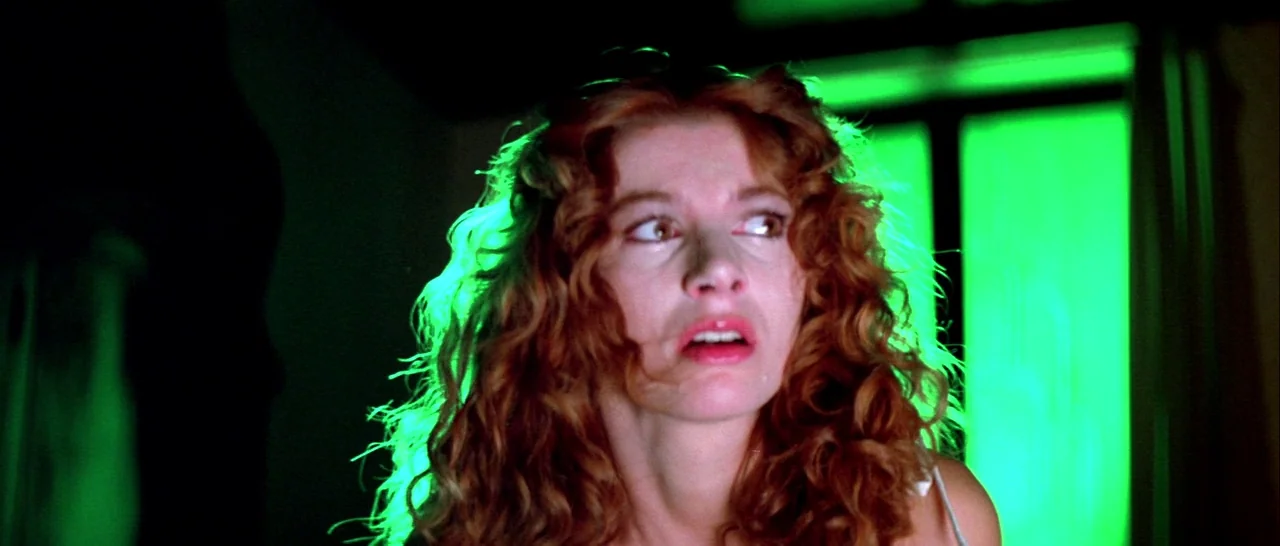 Suspiria (1977) movie still: closeup — A dark room illuminated only by an intense green light from a window. A woman with long curly hair looks…