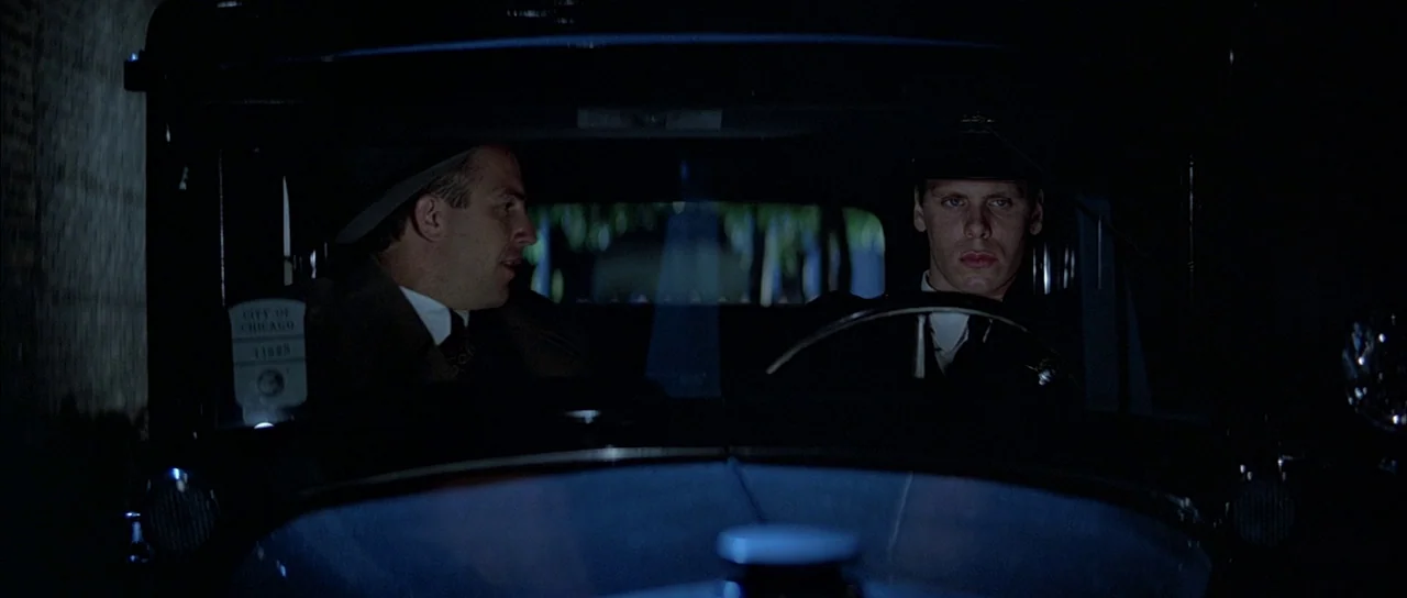 The Untouchables (1987) movie still: medium — The interior of a 1930s vehicle at night is bathed in heavy, dark shadows. Two men in…