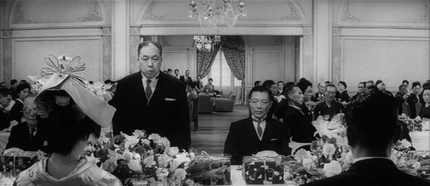The Bad Sleep Well (1960) movie still: medium — A spacious, elegant banquet hall features chandeliers and white-covered tables filled with floral…