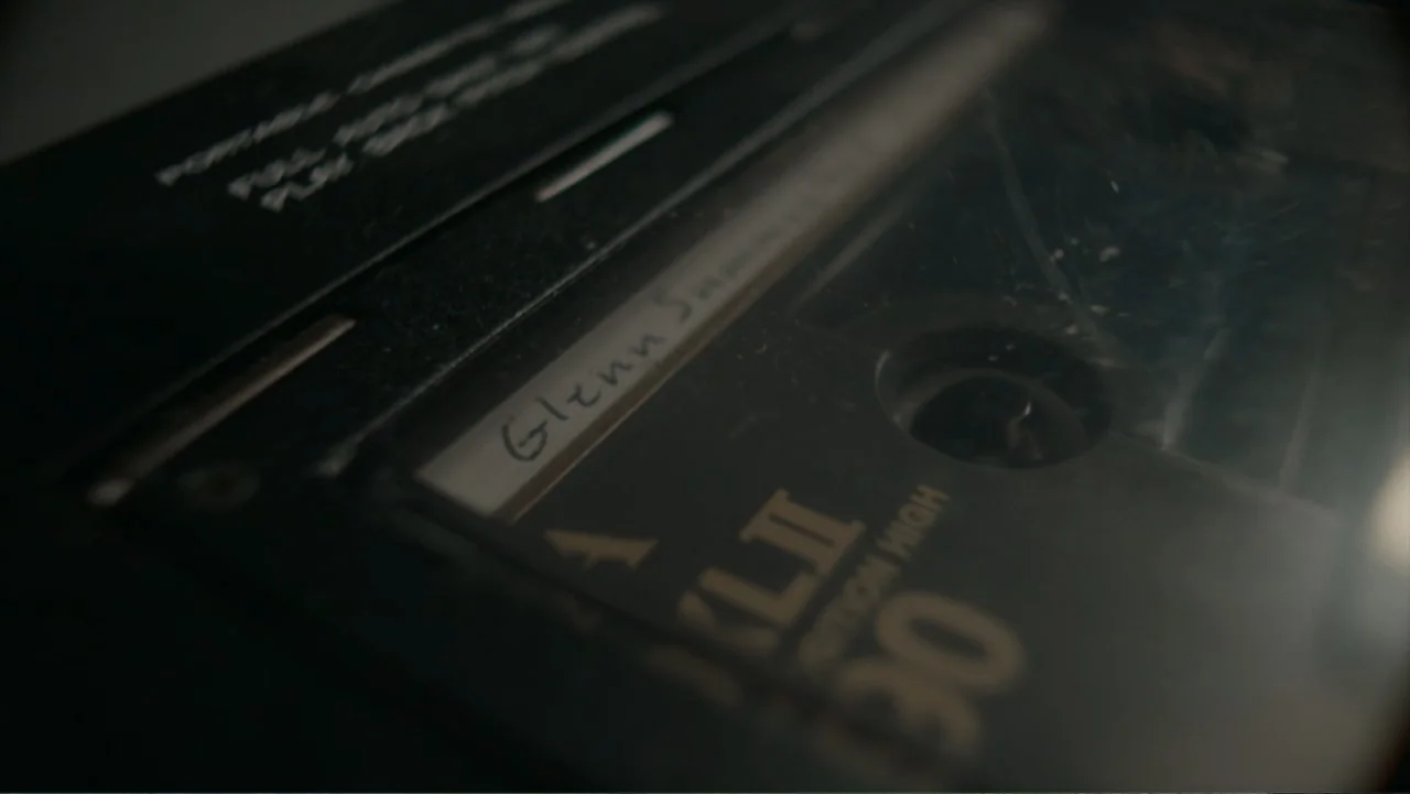 Alabama Snake (2020) movie still: closeup — A close-up view shows a black audio cassette resting inside a portable tape player. The handwritten…