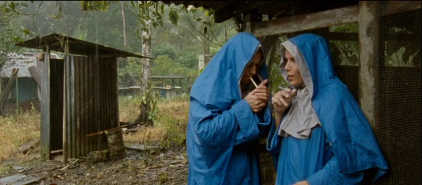 Mister Lonely (2007) movie still: medium — A rural setting with a corrugated metal structure visible in the background rain. Two women in blue…