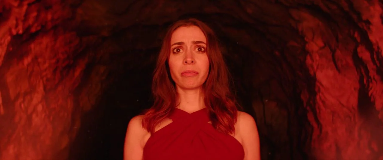 Palm Springs (2020) movie still: medium — A dark rocky cave interior with irregular walls and stone textures. A young woman stands centered in the…