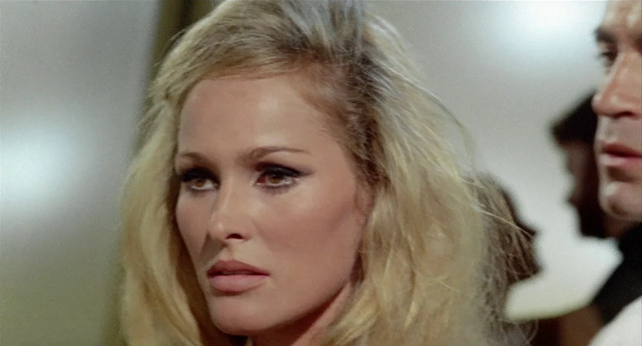 The 10th Victim (1965) movie still: closeup — An interior space with a neutral, slightly out-of-focus background. A blonde woman occupies the center…